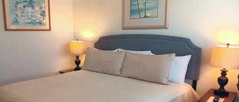 A neatly made bed with a patterned bedspread, two bedside lamps, and two framed pictures on the wall.