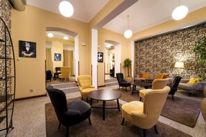 A hotel lobby with a seating area, a staircase, and a wall with a floral pattern. - EA Hotel Victoria (Prague)