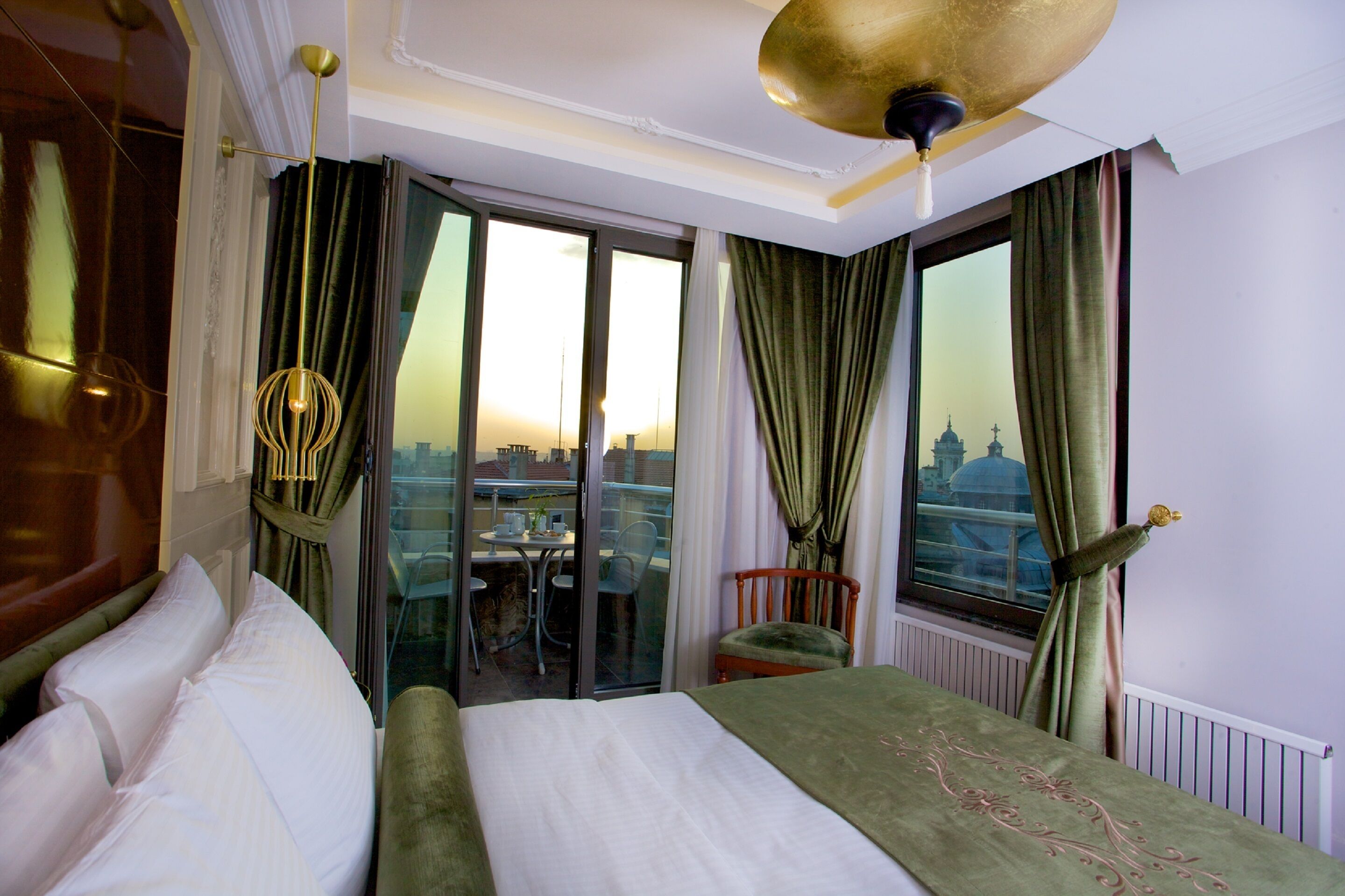 A hotel room with a bed, a chair, a table, and a view of a cityscape through large windows.