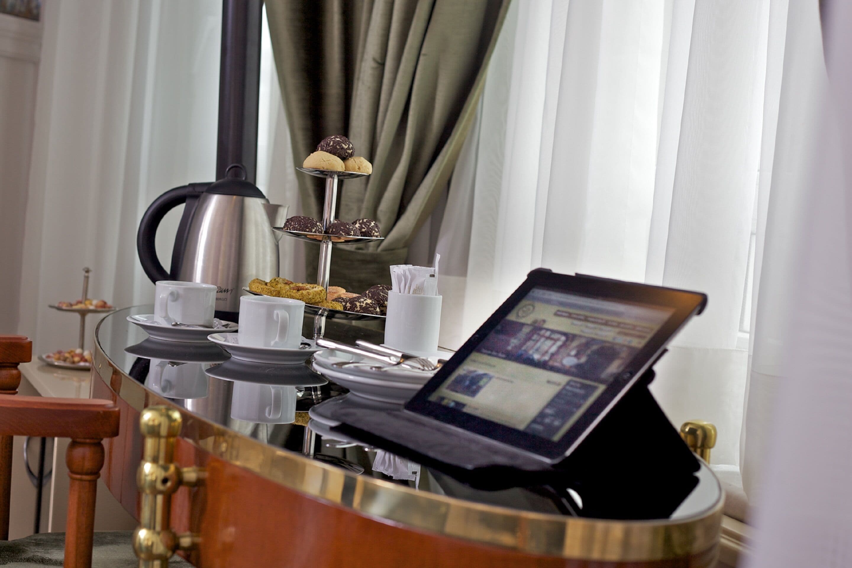 Colazione allestita con un laptop su un tavolo in vetro, una caffettiera e un vassoio per dolci.