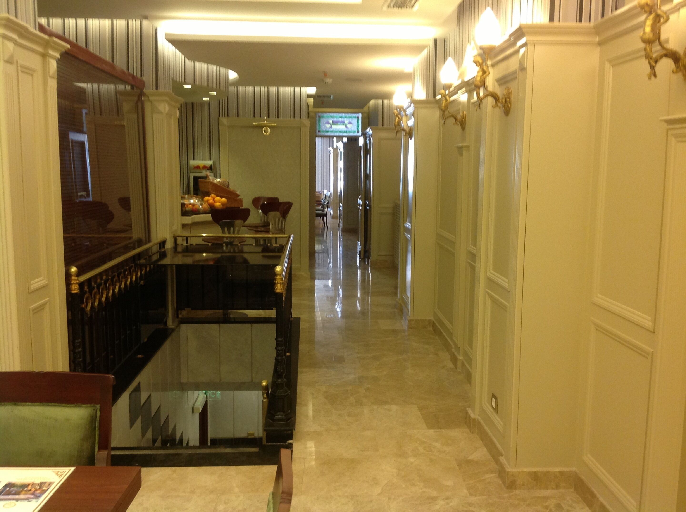 Un couloir d’hôtel avec un comptoir de réception, un espace repas avec une table et des chaises, et un long couloir avec des portes.