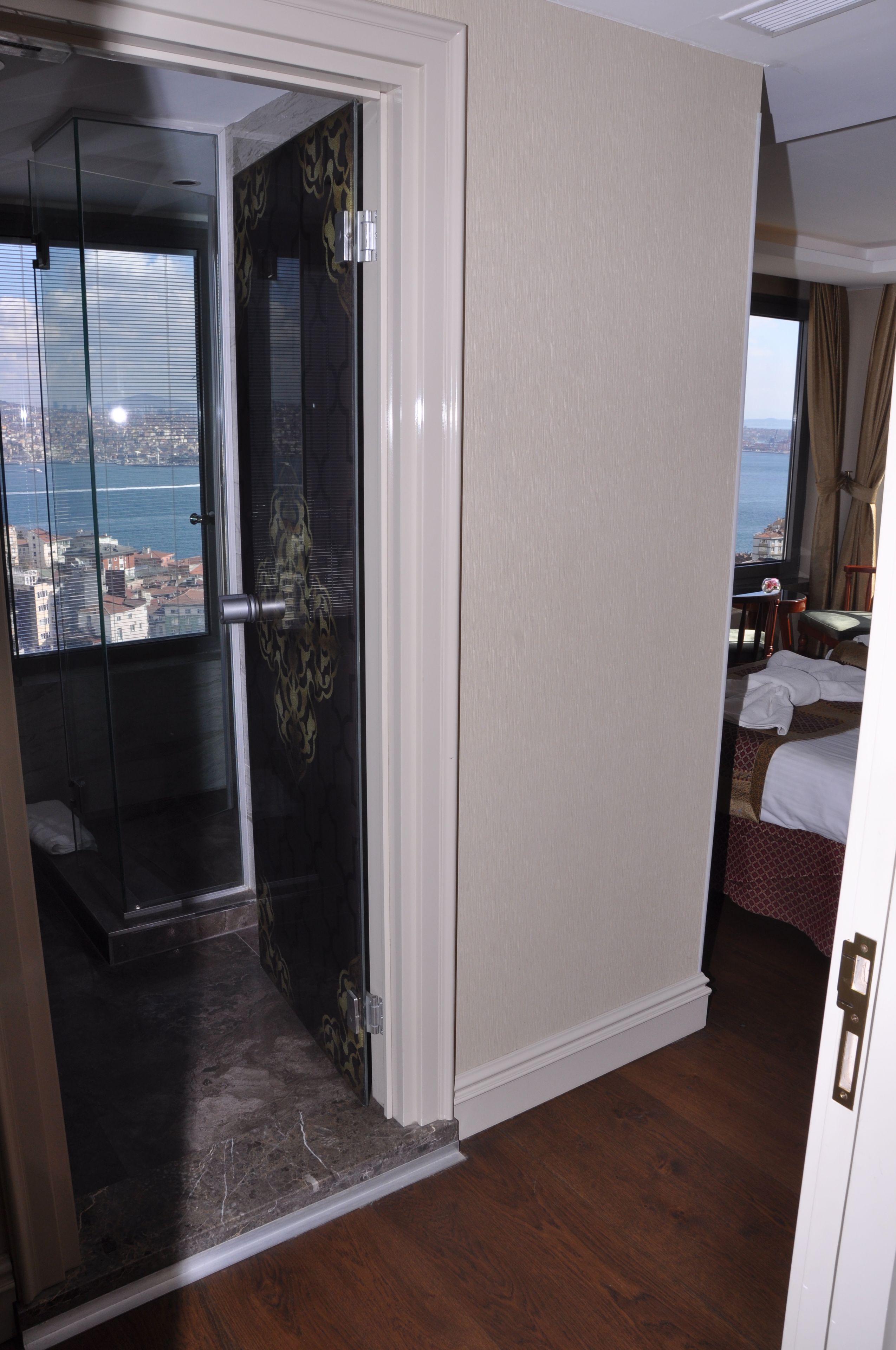 A hotel room with a balcony, a bed, a desk, and a view of the city.