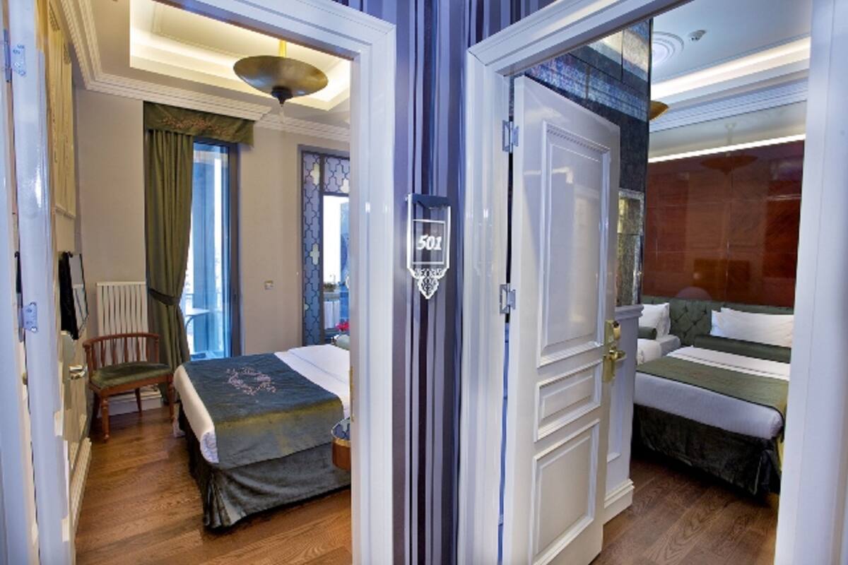 A hotel room with two beds, a wooden floor, a chandelier, and a view of the city.