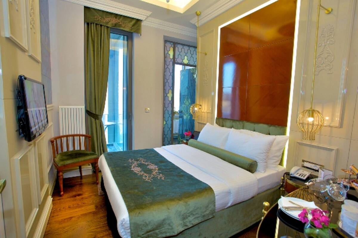 A hotel room with a large bed, a wooden chair, a desk with a telephone, and a vase with flowers.