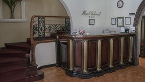 Uma área de recepção com balcão de madeira, um relógio, certificados emoldurados e uma escadaria com tapete vermelho.