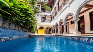 Uma piscina com bordas azulejadas, rodeada por um edifício com varandas e arcadas.