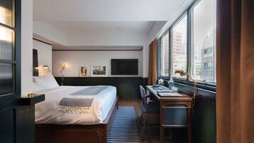 Habitación de hotel con cama, escritorio y amplios ventanales con vistas a la ciudad.
