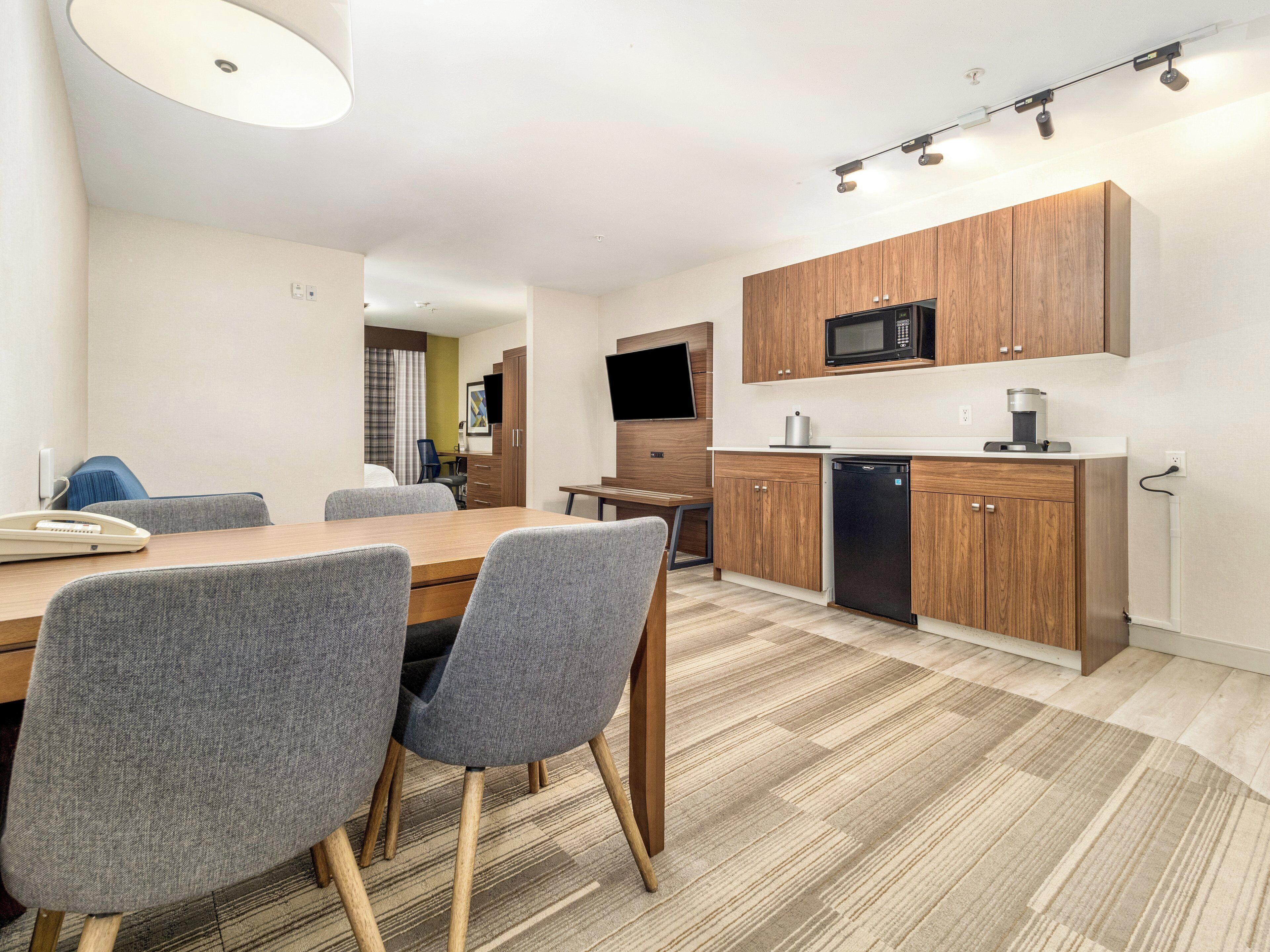 Una cocina moderna con armarios de madera, un microondas y un lavavajillas. Hay un comedor con mesa y sillas.