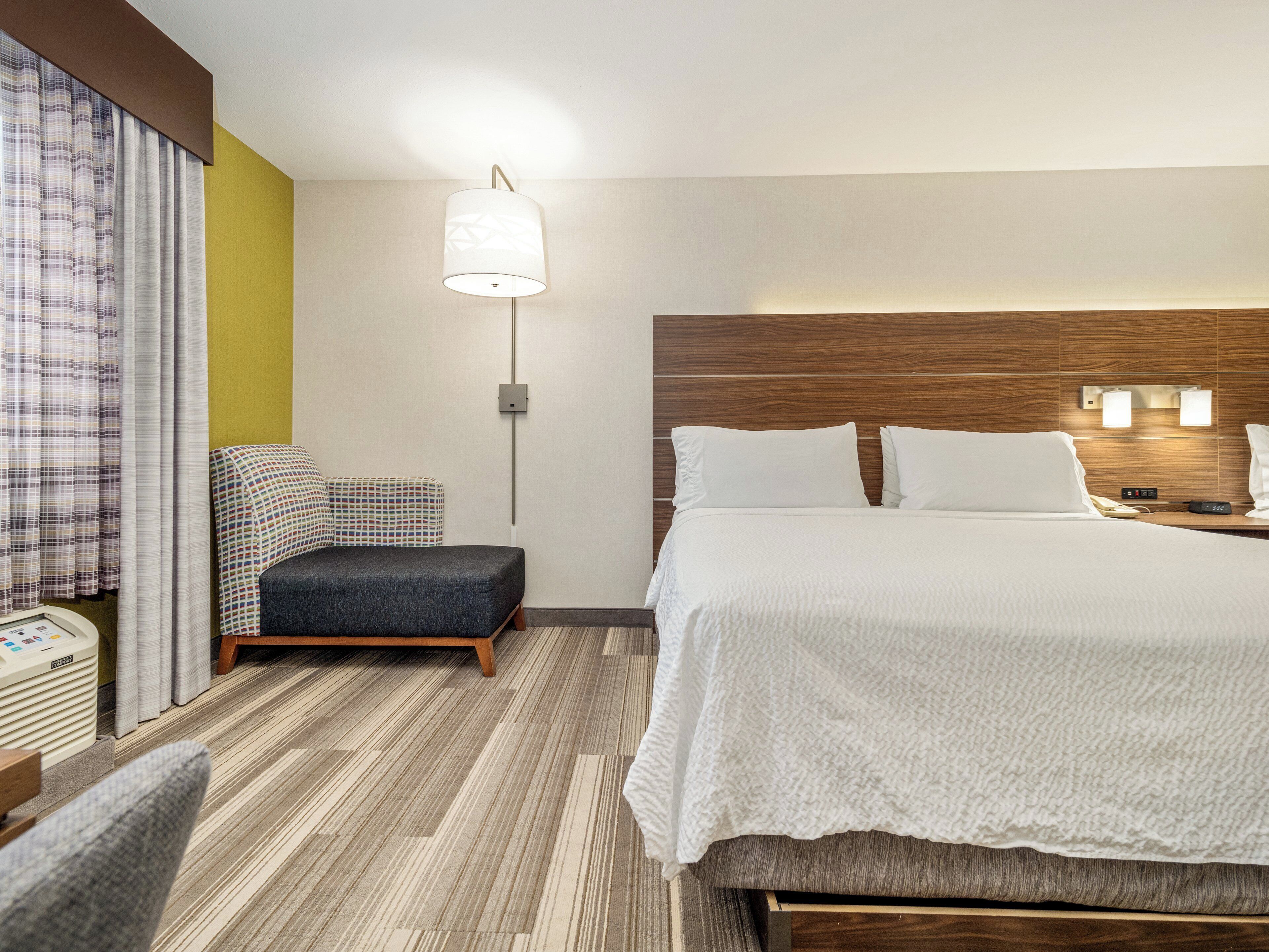 Habitación de hotel con una cama grande, una mesita de noche con lámpara, una silla y una pequeña mesa con teléfono.