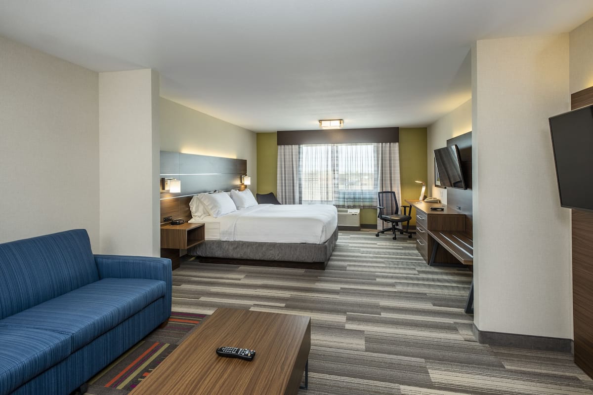 Une chambre d’hôtel avec un lit, un canapé bleu, un bureau avec une chaise, une télévision et une fenêtre avec des rideaux.