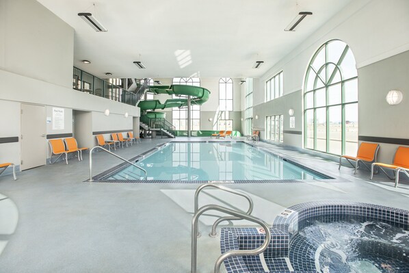 An indoor swimming pool with a hot tub, multiple lanes, and orange chairs.