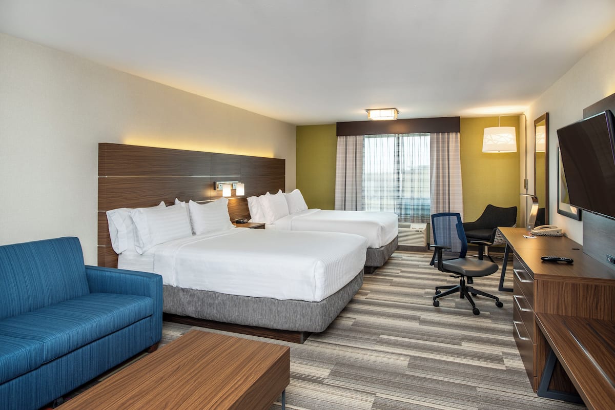 Une chambre d’hôtel avec deux lits, un canapé, un bureau, une télévision et une fenêtre avec des rideaux.