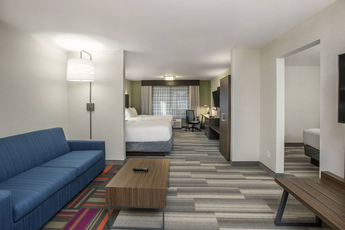 Une chambre d’hôtel avec un canapé bleu, une table basse en bois, un lit, un bureau avec une chaise et un téléviseur.