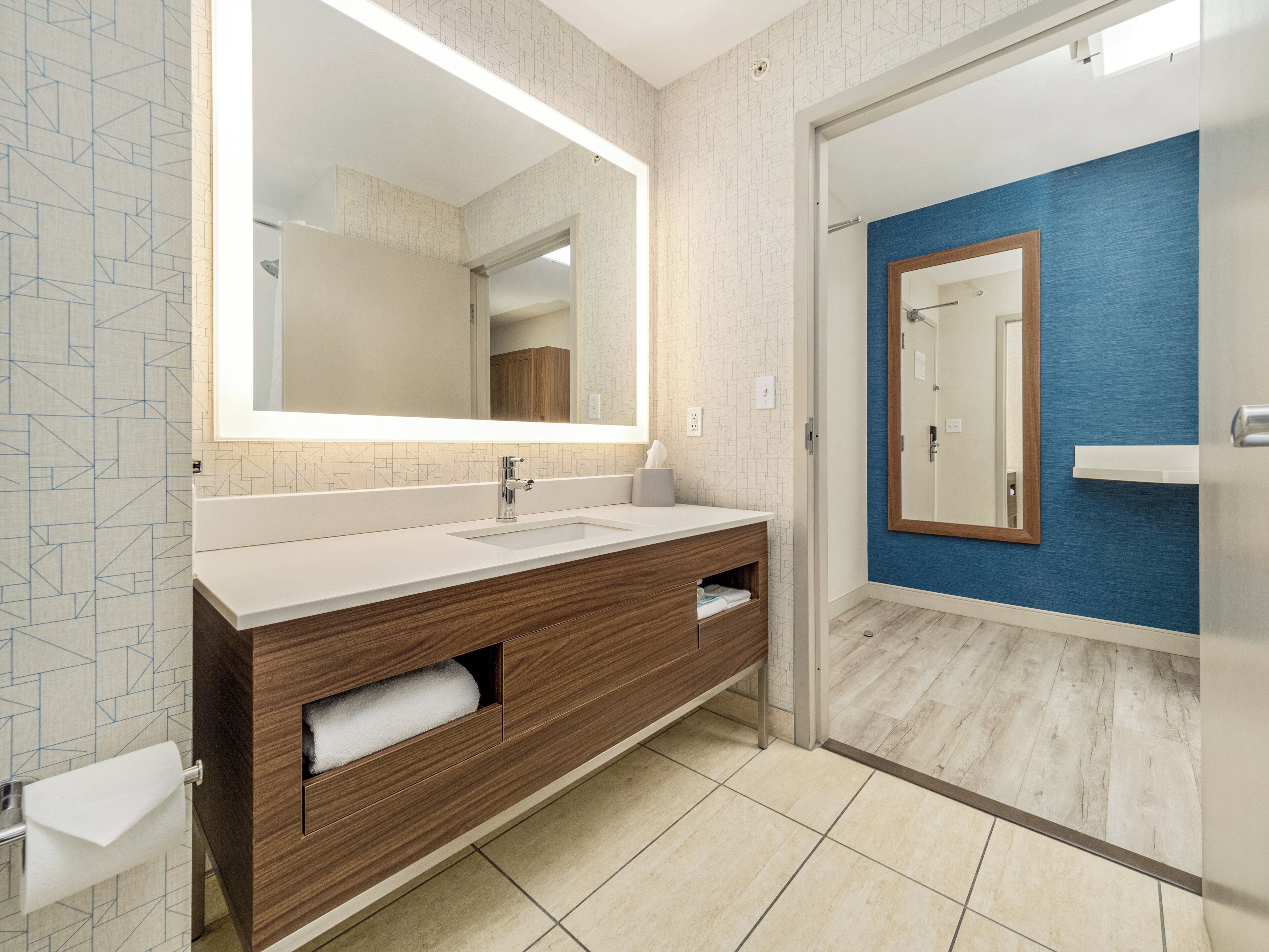 Un baño moderno con un espejo grande, un lavamanos y un mueble de tocador con espacio de almacenamiento.