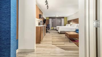Una habitación de hotel con un escritorio de madera, una cama, un televisor y un ventanal con cortinas.