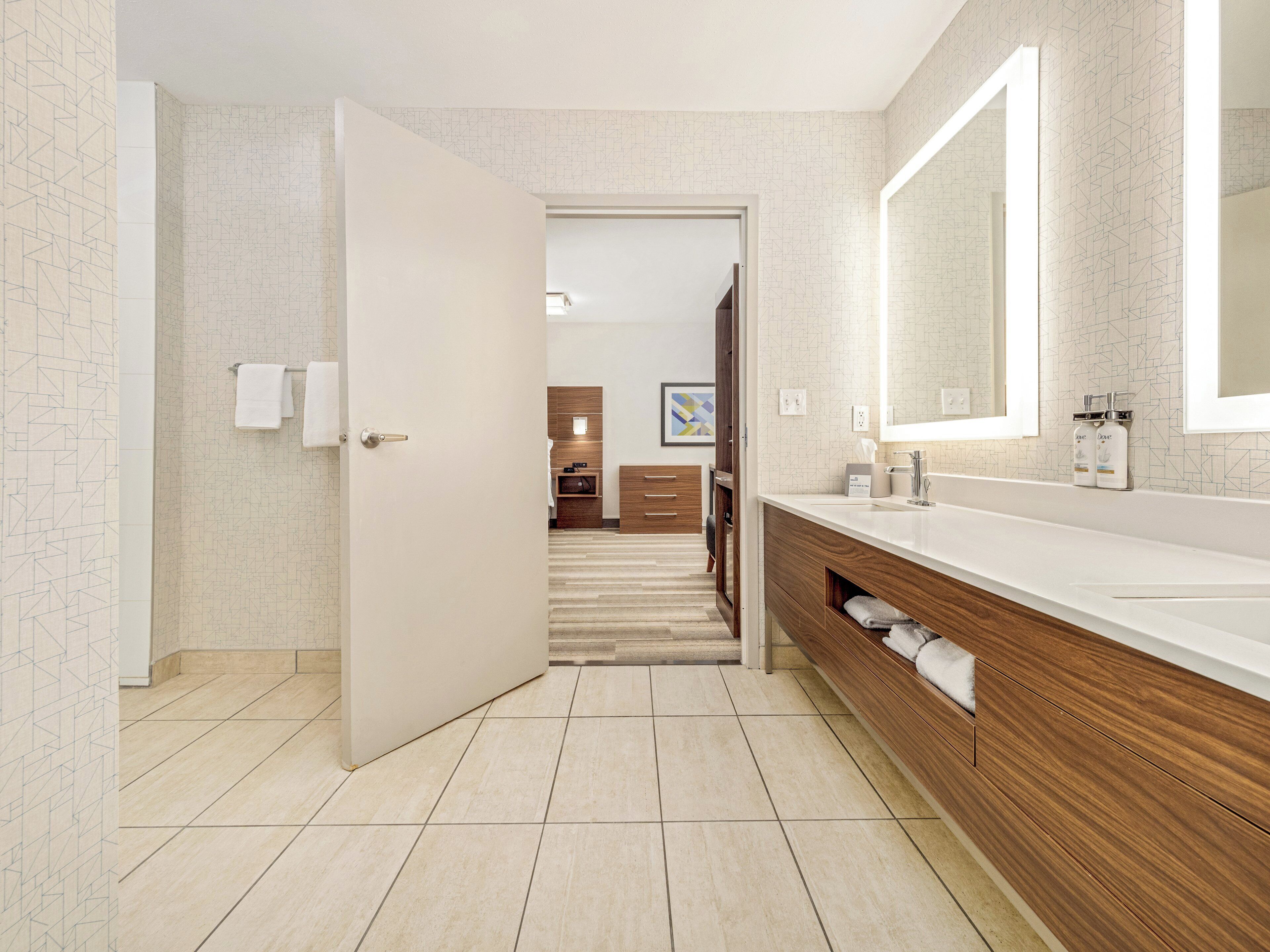 A modern bathroom with a large mirror, wooden vanity, and a shower area.