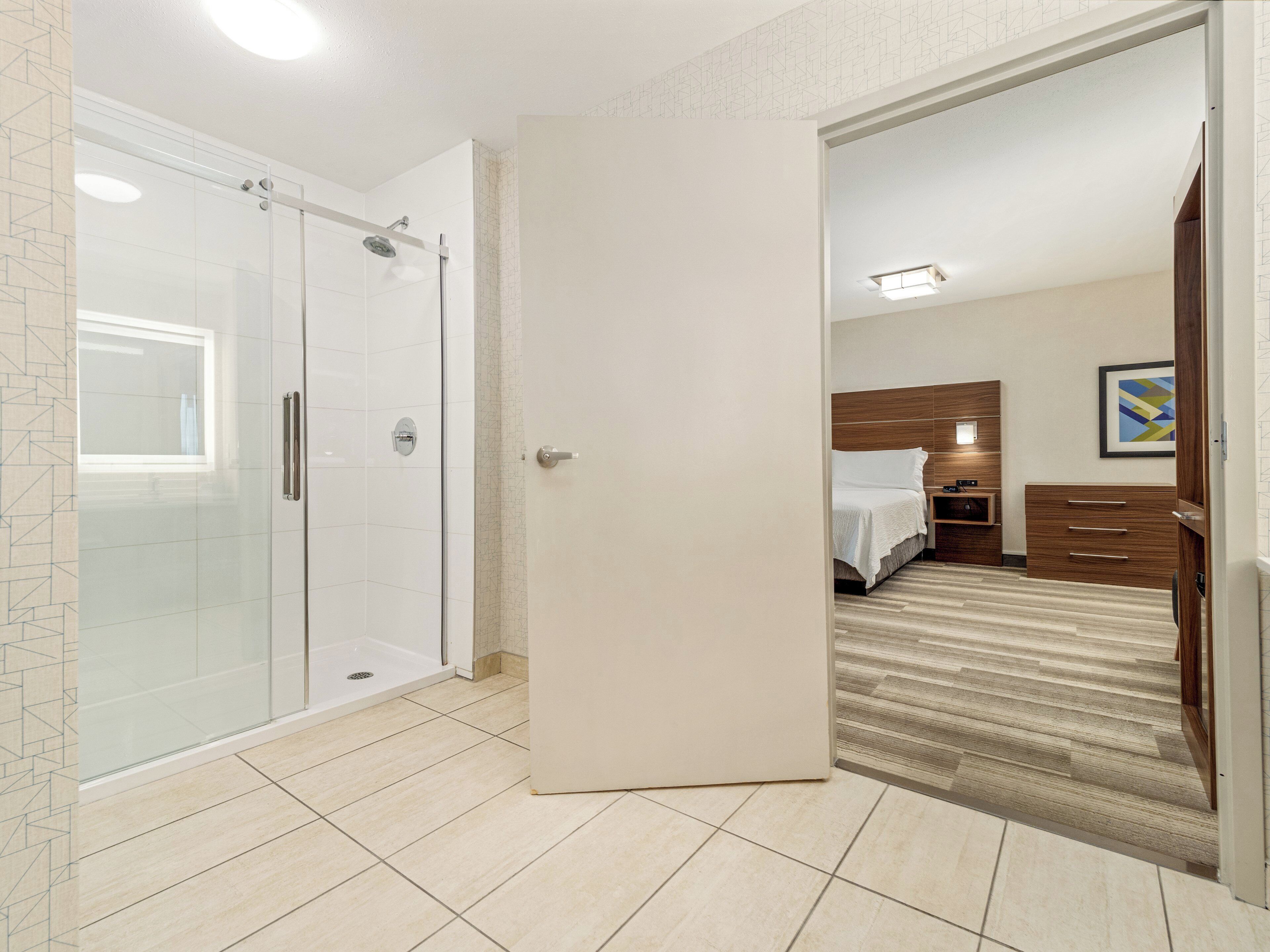 A hotel room with a glass-enclosed shower, a bed with a wooden headboard, and a carpeted floor.