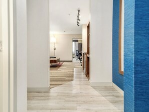 Een hotelgang met een houten vloer, een bureau met stoel, een lamp en een blauwe accentmuur.