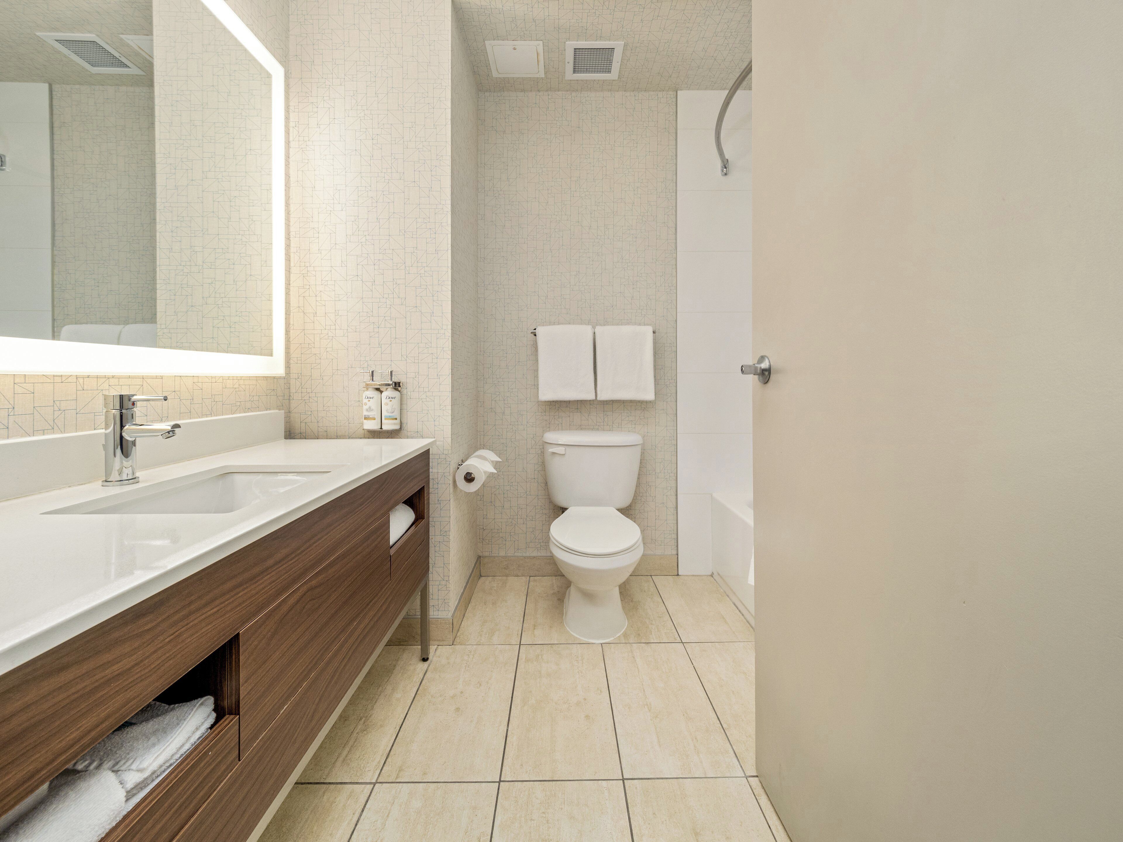 A modern bathroom with a large mirror, two sinks, a toilet, and a shower.