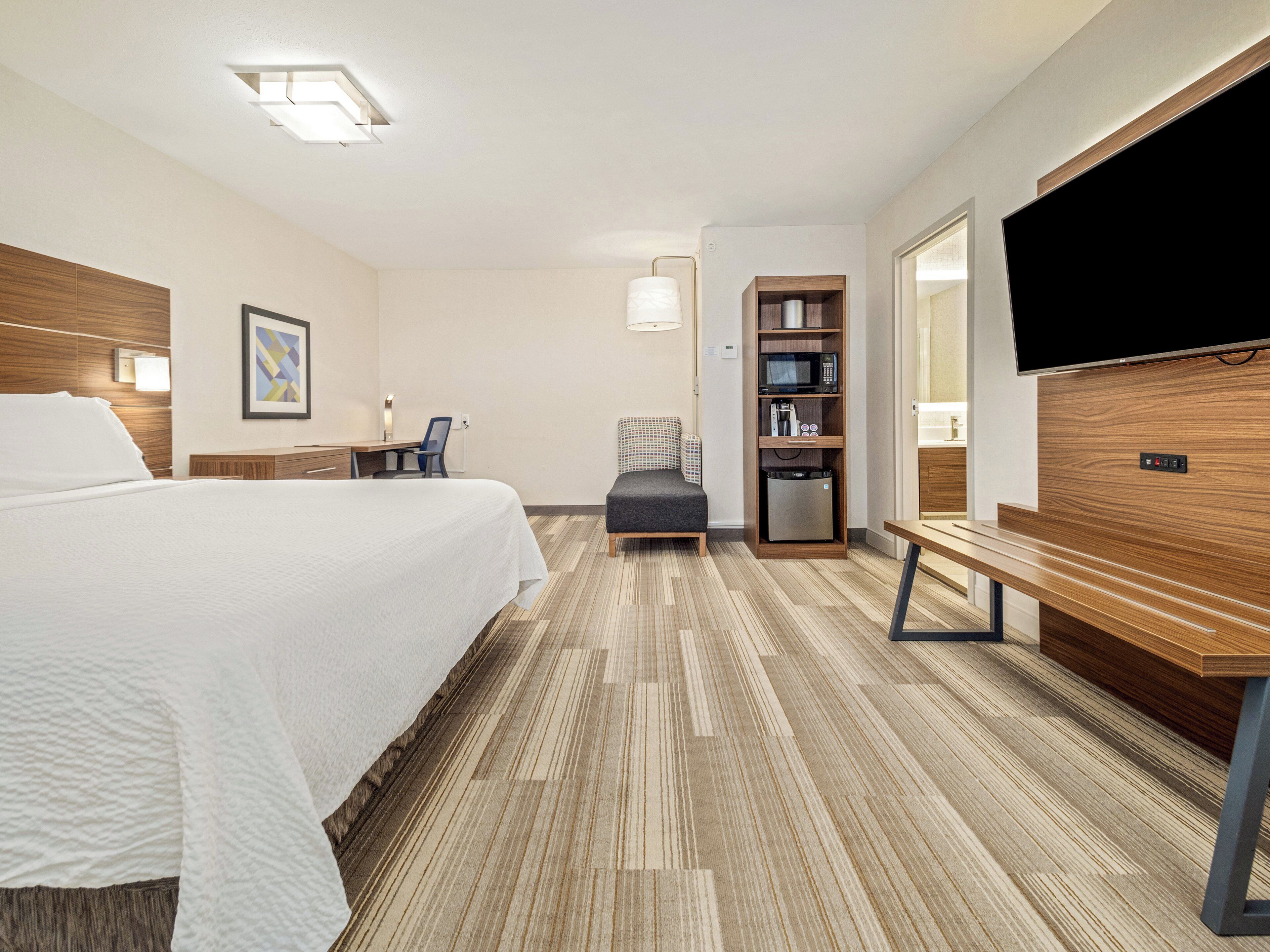 A hotel room with a large bed, a desk, a chair, a small sofa, a TV, a microwave, and a mini-fridge.