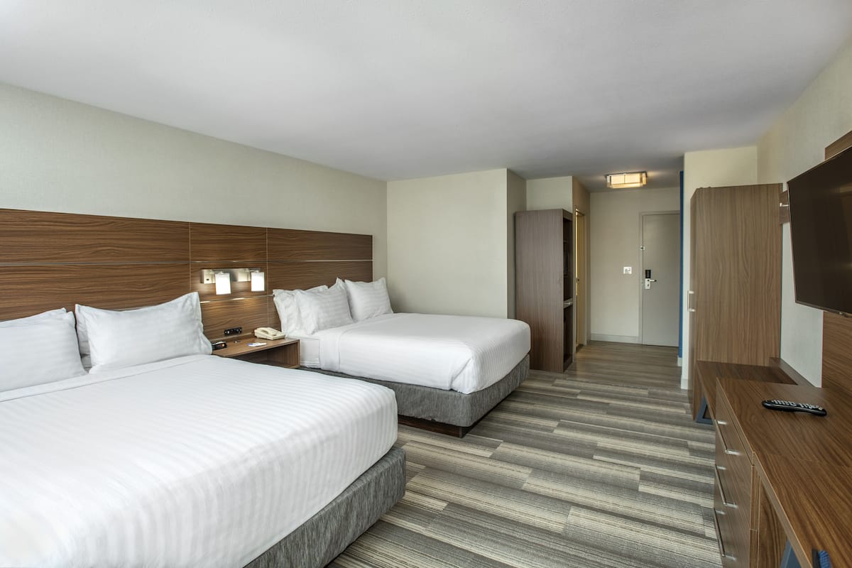Une chambre d’hôtel avec deux lits, une tête de lit en bois, un bureau avec un téléphone et un téléviseur posé sur un meuble en bois.
