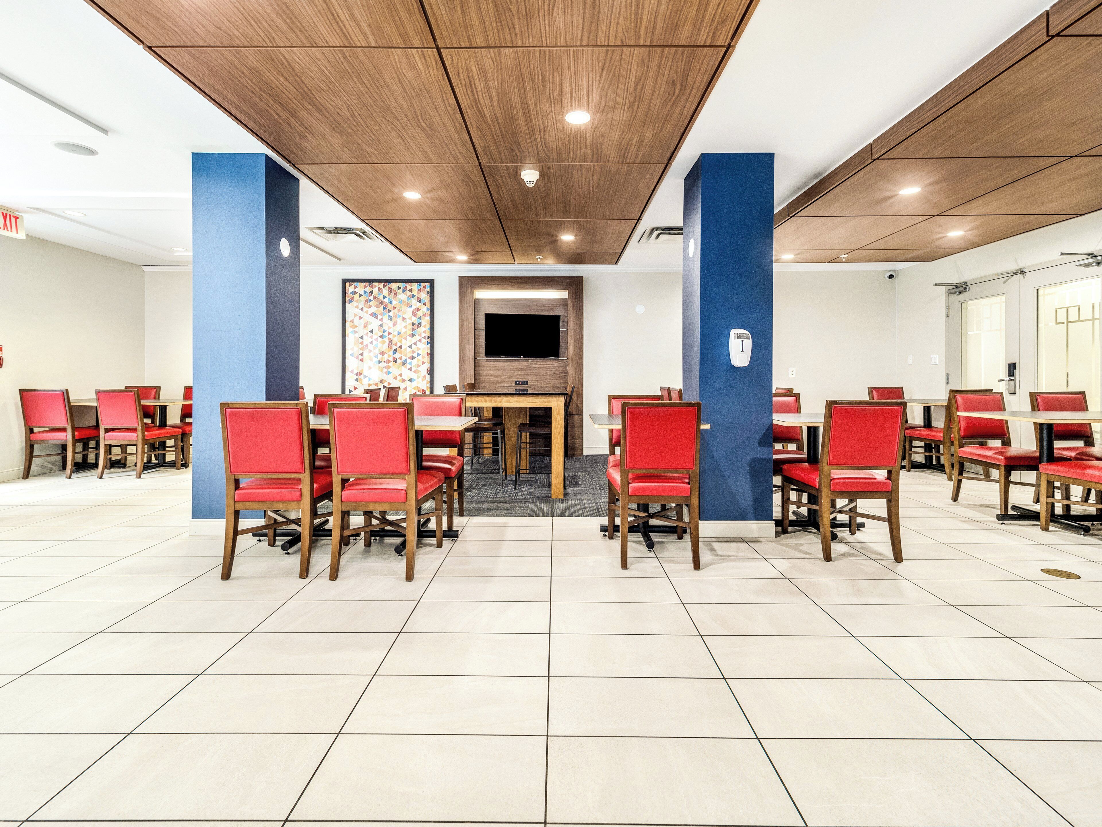 Een vergaderzaal met rode stoelen, een groot scherm en een houten plafond.