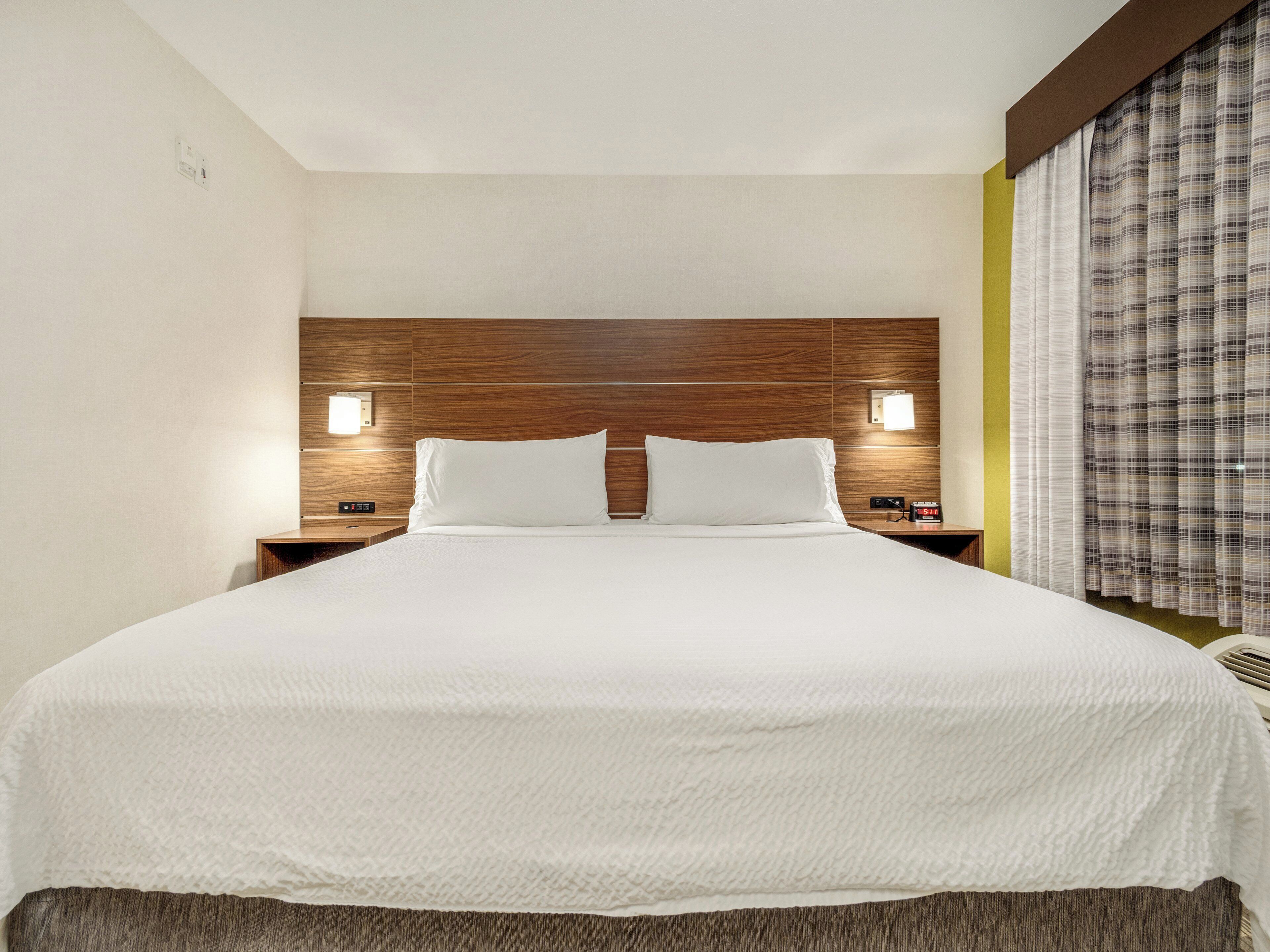 A hotel room with a large bed, wooden headboard, bedside lamps, and a window with curtains.