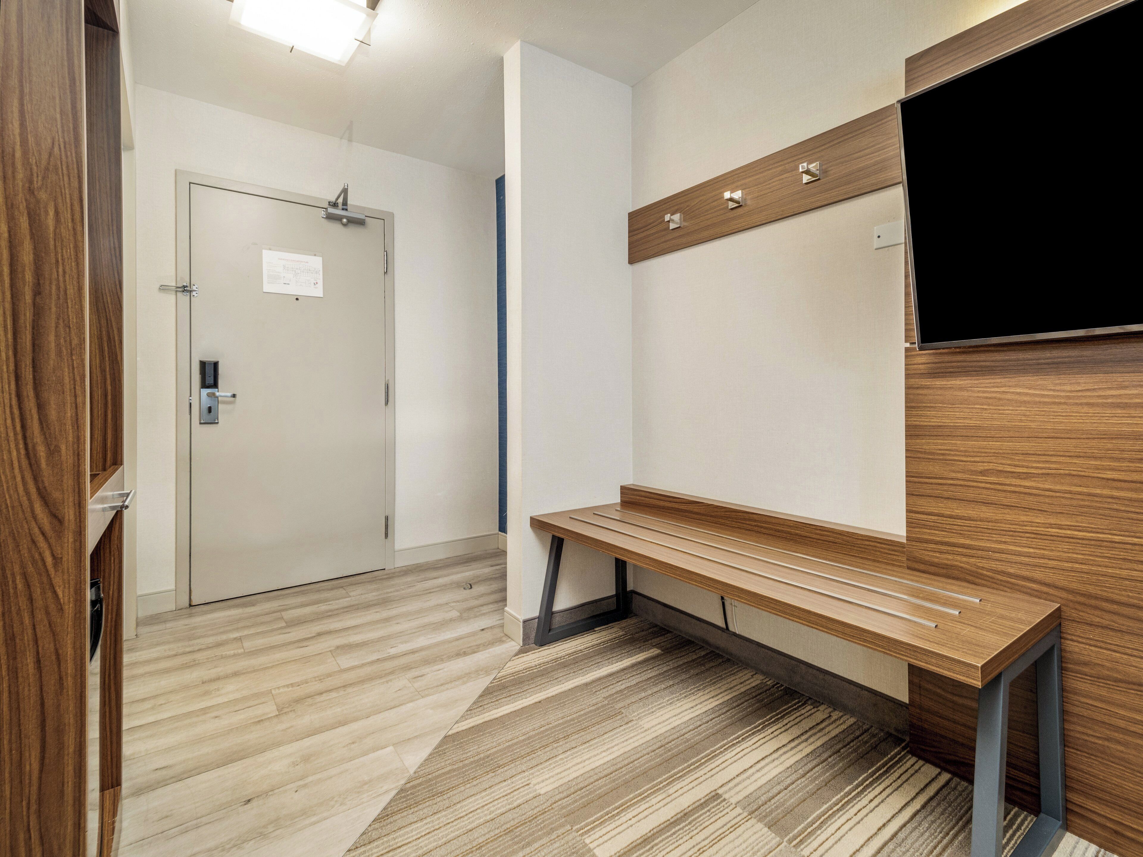 Un pasillo con un banco de madera, una puerta y un televisor en la pared.