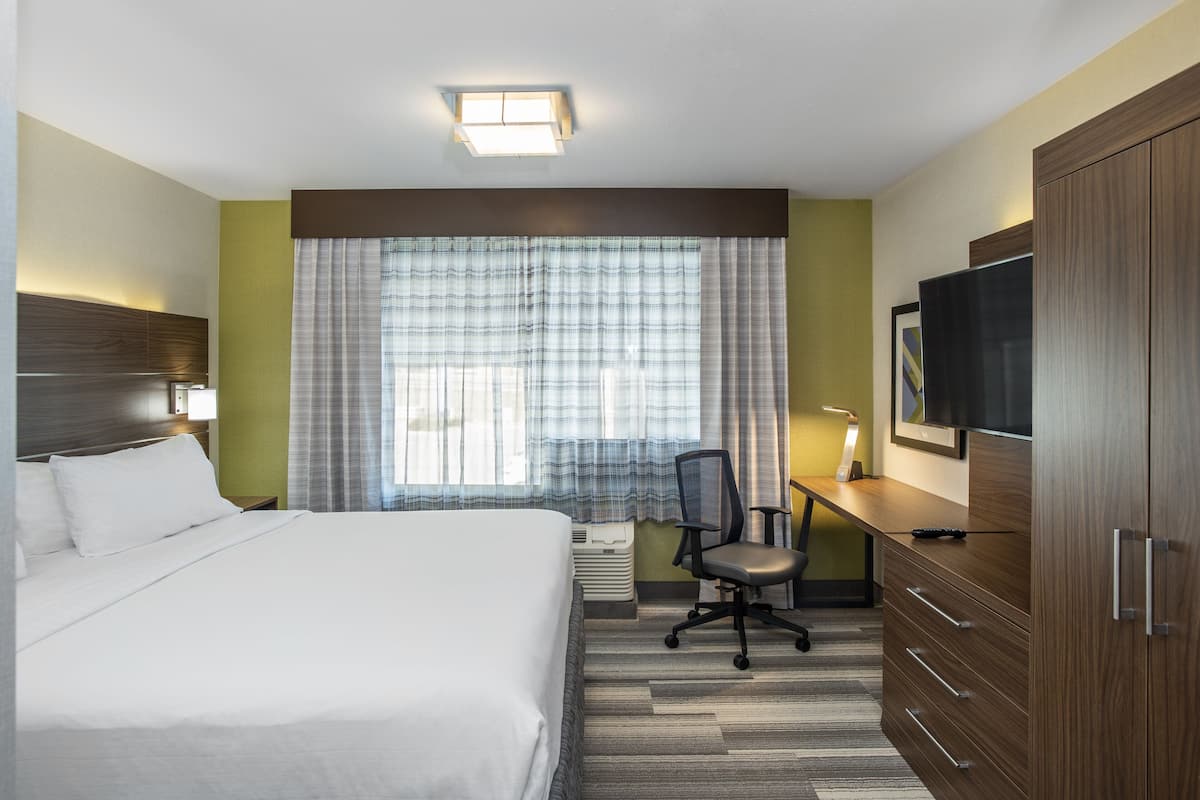 Une chambre d’hôtel comprenant un lit, un bureau avec une chaise, une télévision et une armoire.