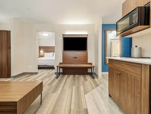 A modern hotel room with a wooden floor, a bed with white bedding, a flat-screen TV mounted on the wall, a microwave above the counter, and a small table. - Holiday Inn Express & Suites Medicine Hat Transcanada Hwy 1 by IHG (Medicine Hat)