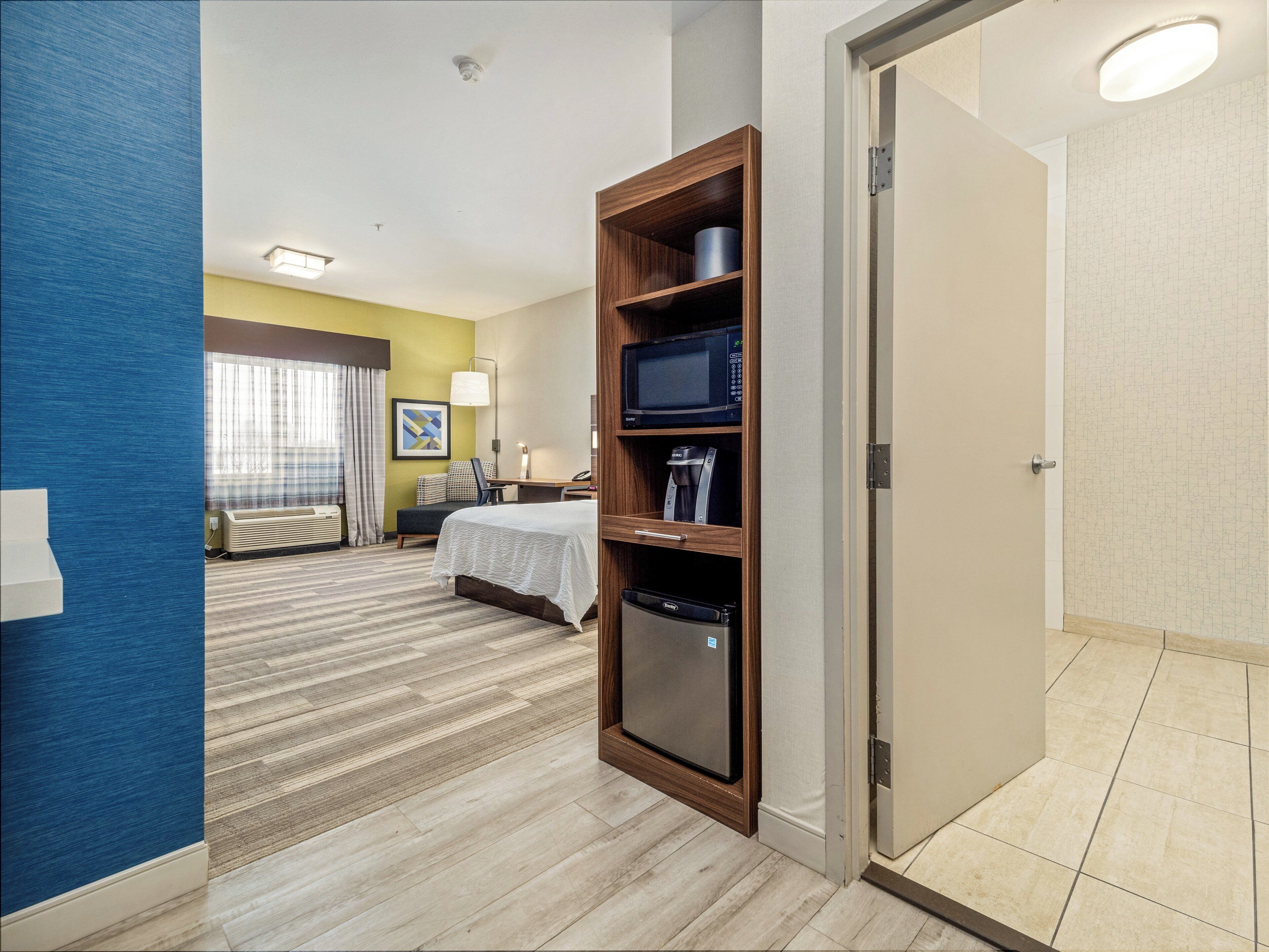 A hotel room with a bed, a desk, a chair, a microwave, and a minibar.