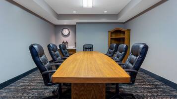 Un salón de conferencias con una mesa de madera, sillas de cuero negro, un reloj en la pared y una estantería.