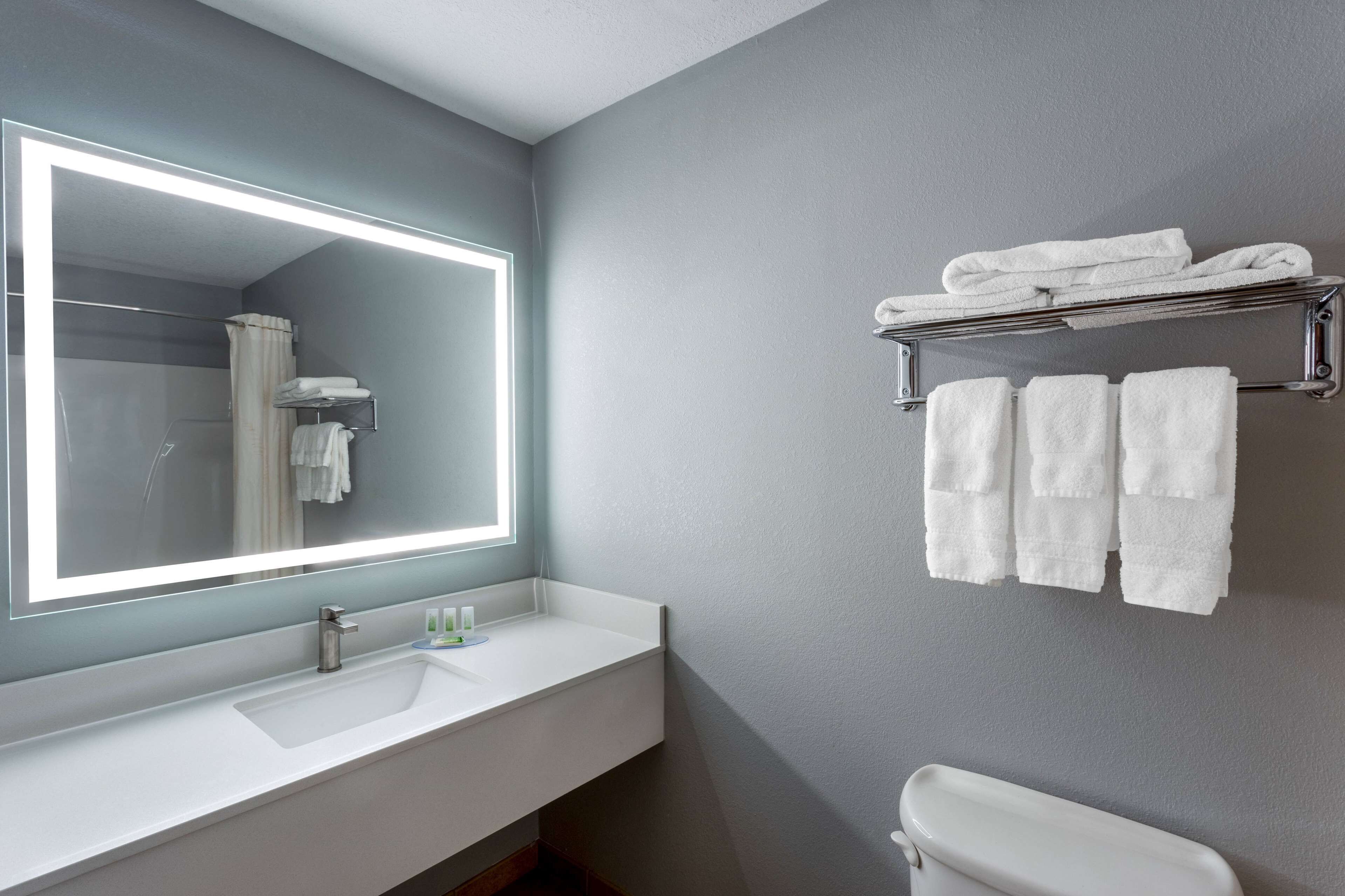Un baño moderno con un espejo grande, lavamanos blanco y un perchero para toallas.