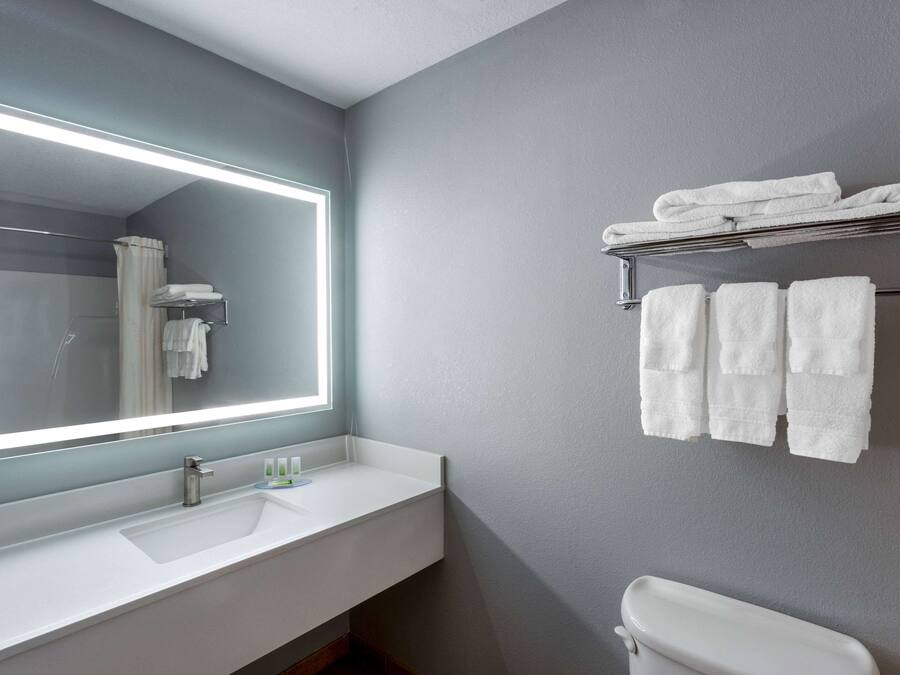 Un baño moderno con un espejo grande, lavamanos blanco y un perchero para toallas.