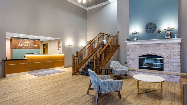 Un vestíbulo de hotel con mostrador de recepción, una escalera, zona de estar y chimenea.
