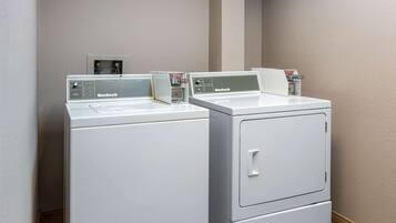 Two white Huebsch front-loading washing machines in a laundry room with a beige wall and a power outlet visible.