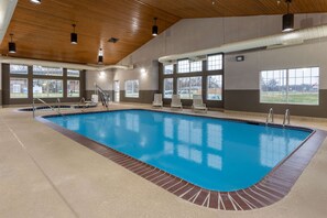 An indoor swimming pool with clear windows, a wooden ceiling, and a tiled border.