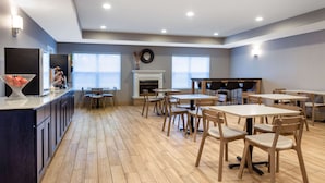 Un comedor amplio con varias mesas y sillas, una chimenea central y ventanas grandes que ofrecen luz natural.