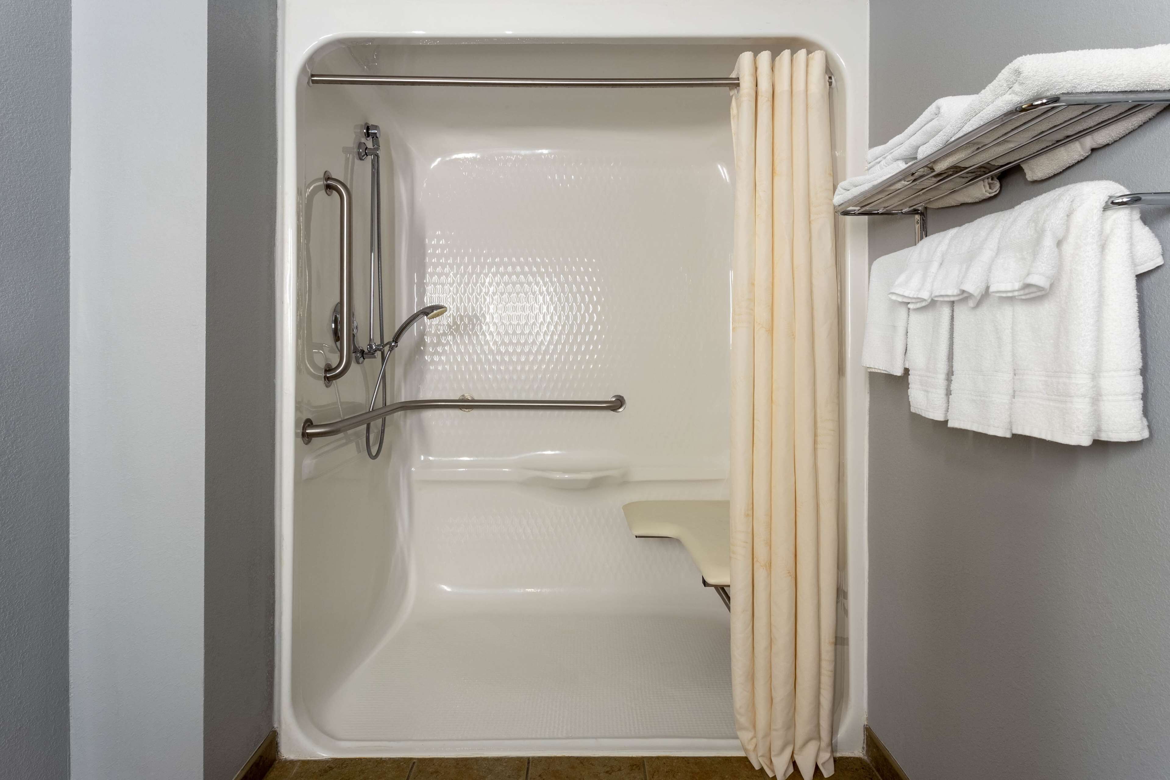 A bathroom with a bathtub, grab bars, a towel rack, and a shower curtain.