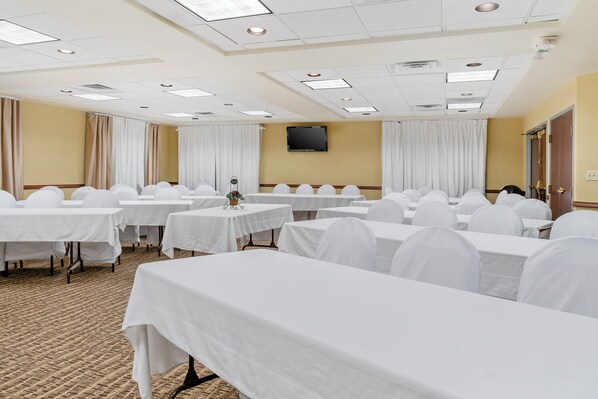A conference room with multiple tables and chairs, a flat-screen TV on the wall, and a carpeted floor.