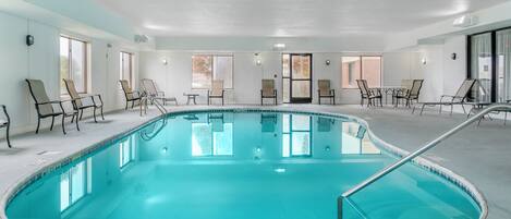Una gran piscina interior con sillones de descanso y mesas alrededor del borde.