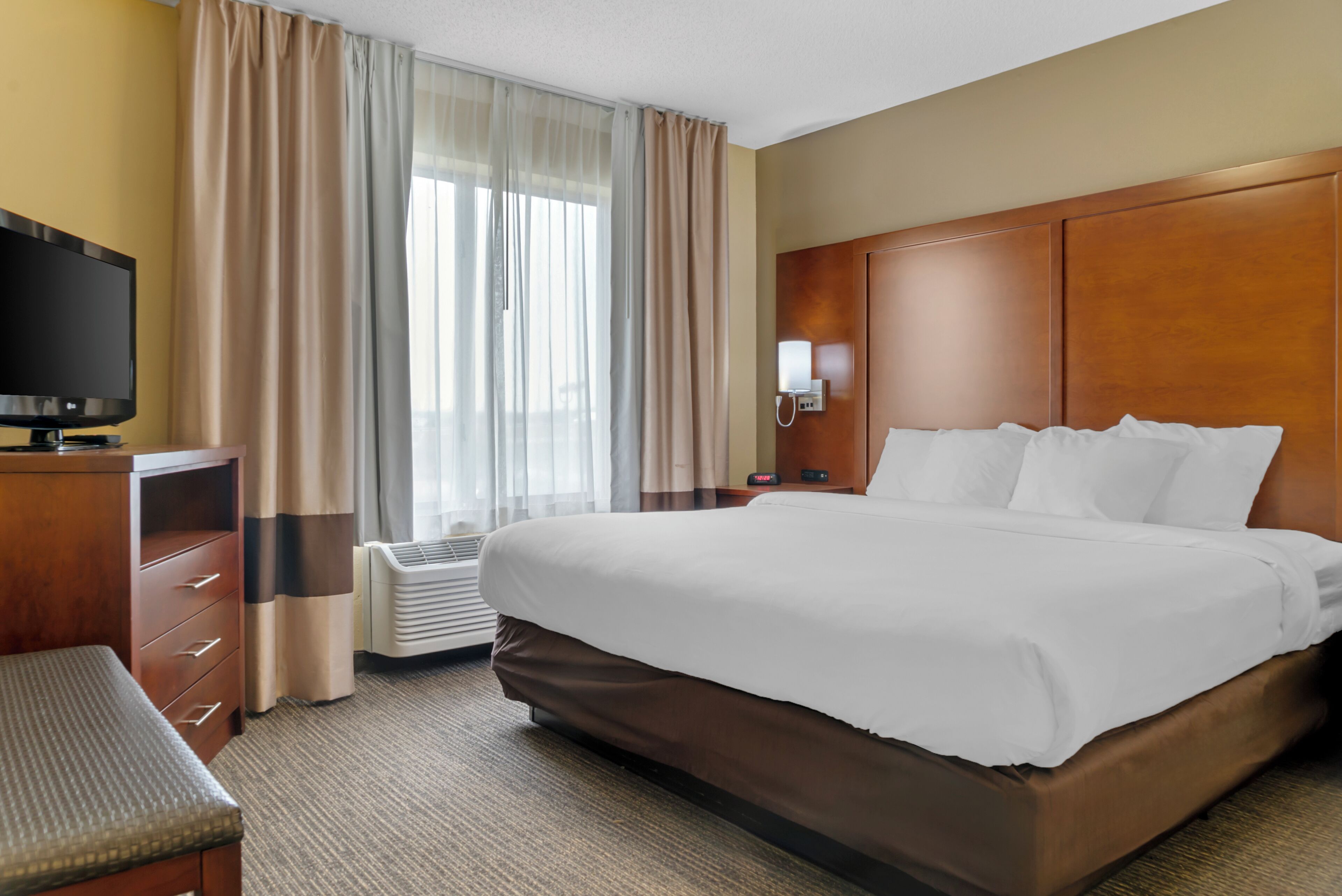 Una habitación de hotel con una cama grande, televisión, escritorio y ventana con cortinas.