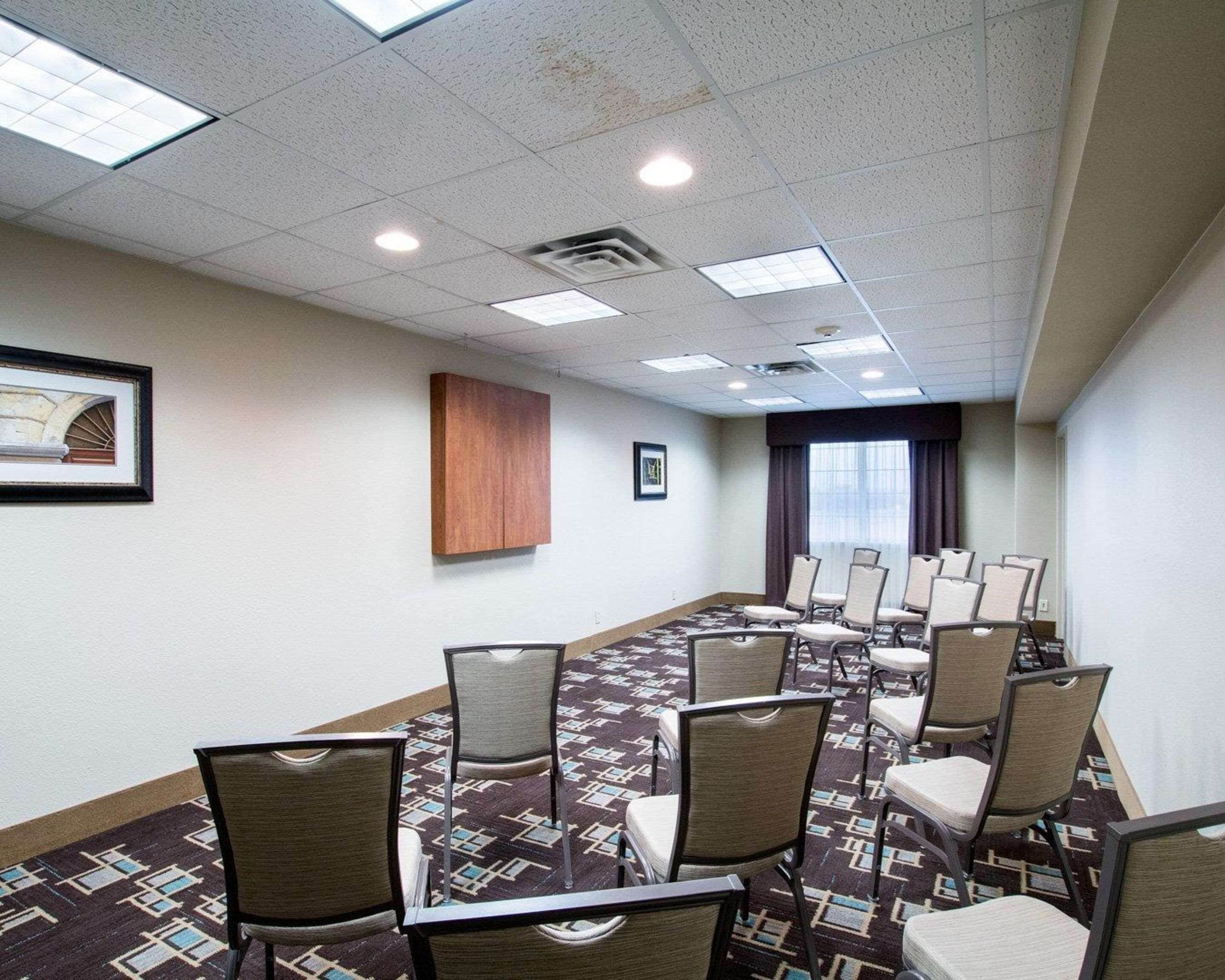 A conference room with rows of chairs, a patterned carpet, and a wooden cabinet.