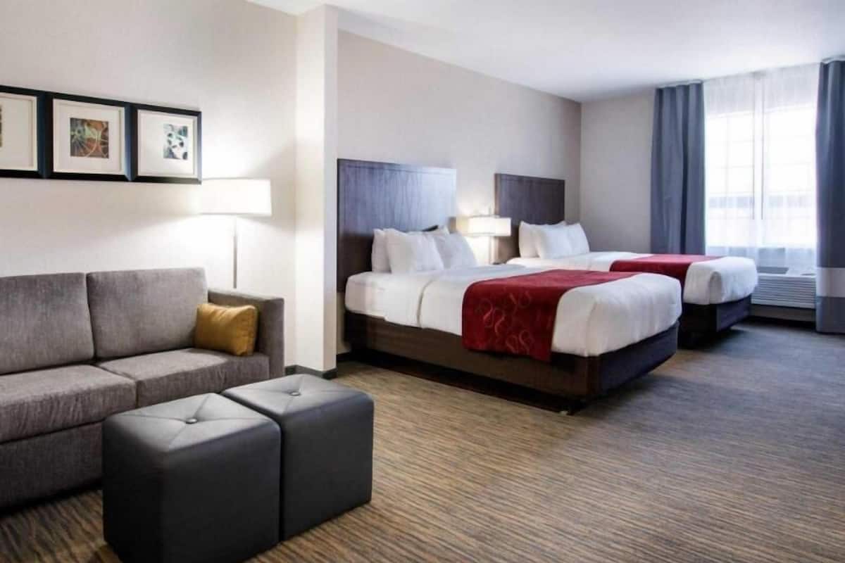 Ett hotellrum med en soffa, två sängar, ett litet bord och ett fönster.