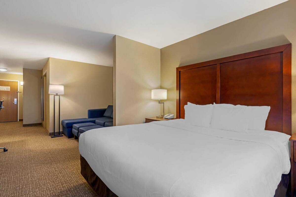 A hotel room with a large bed, a desk with a lamp, a chair, and a sofa.
