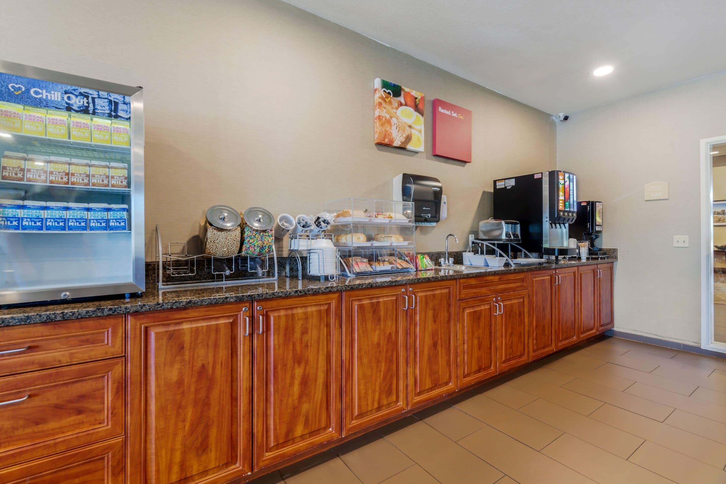 A hotel kitchen with a refrigerator, coffee machines, and a self-serve station.