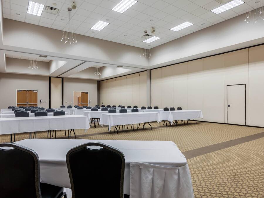 A conference room with rows of tables and chairs, a carpeted floor, and a high ceiling with lighting fixtures.
