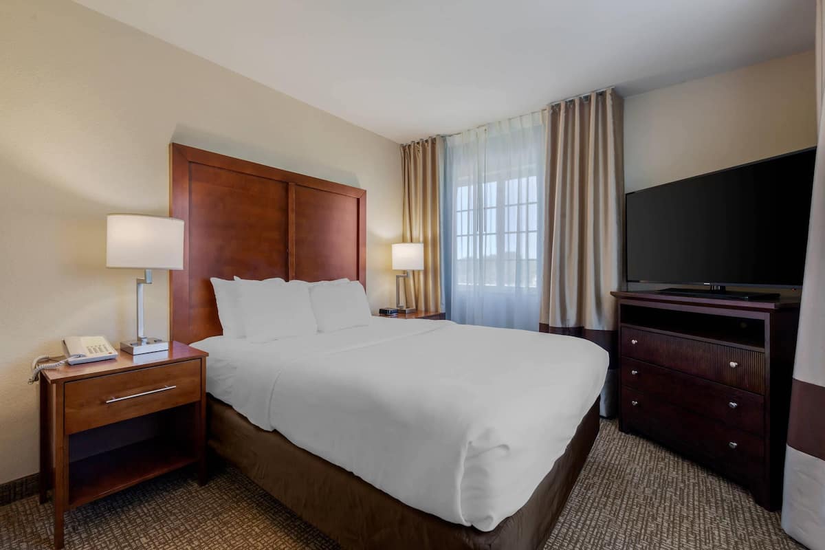 A hotel room with a bed, bedside lamps, a TV, a wooden nightstand, and a dresser.