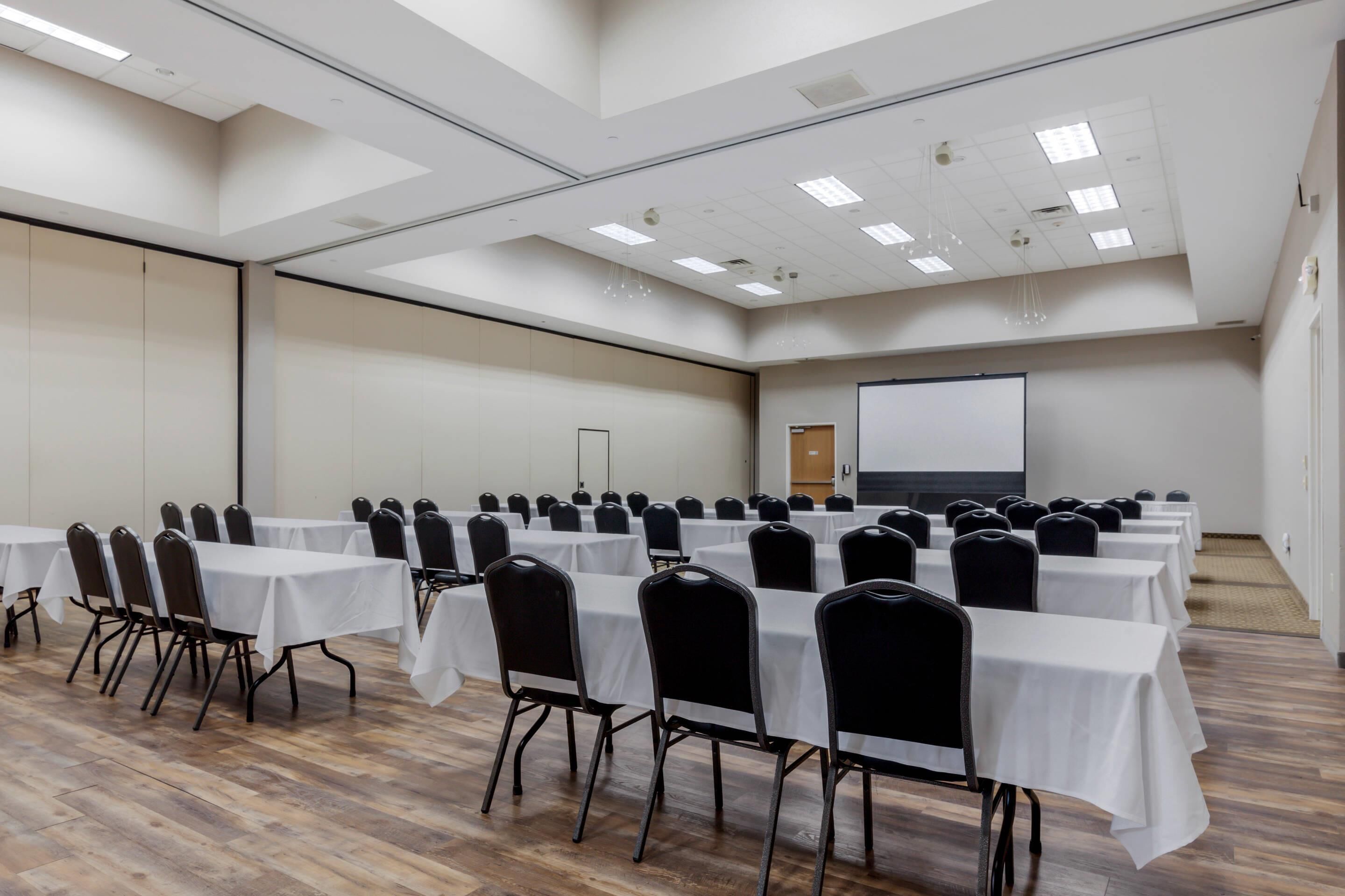 A conference room with multiple tables and chairs, a projector screen, and a large whiteboard.
