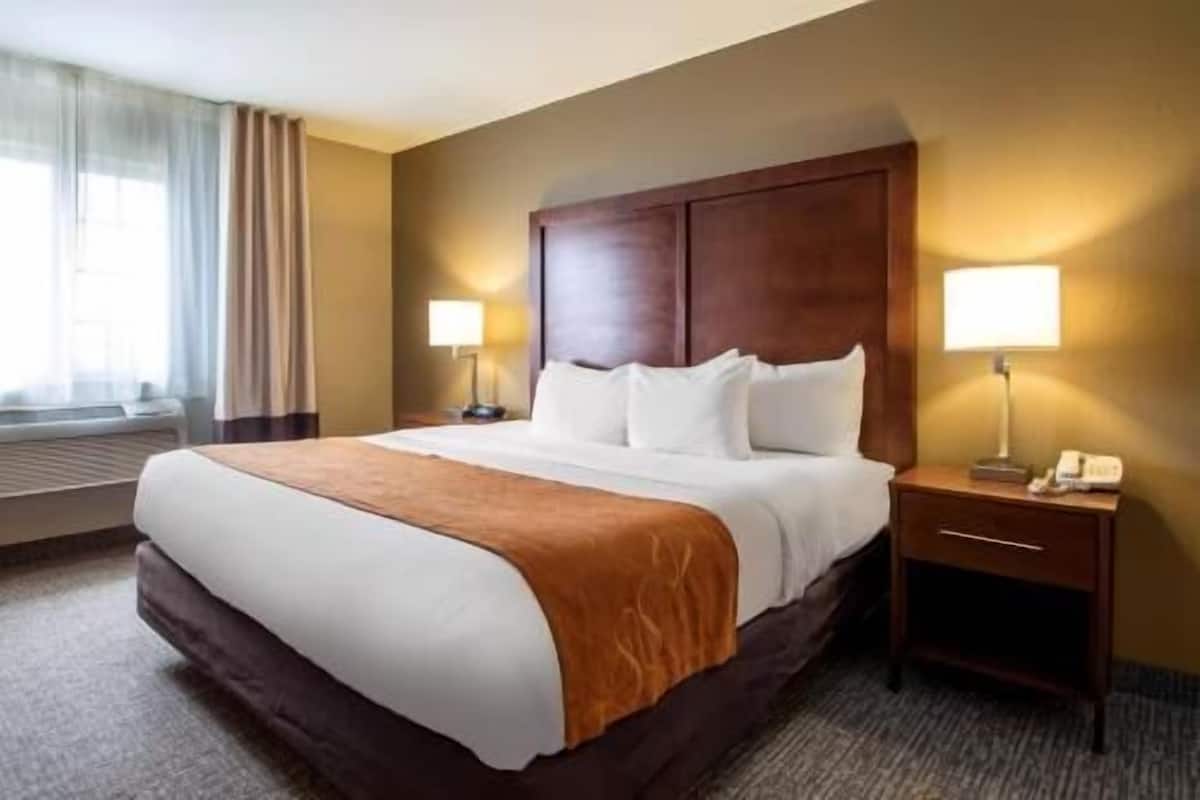 A hotel room with a large bed, two bedside tables with lamps, a window with curtains, and a radiator.